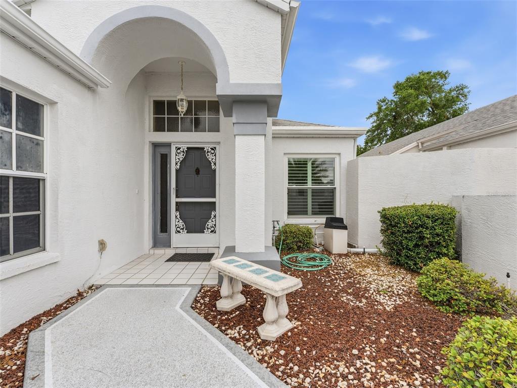 The exterior of a white stucco house features an arched entryway, a stone bench, and landscaping — 10439 CASA GRANDE CIRCLE, SPRING HILL, FL