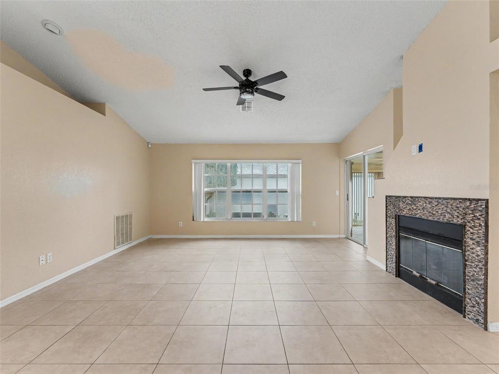 An empty living room features tile flooring, a vaulted ceiling, and a stone-faced fireplace — 10439 CASA GRANDE CIRCLE, SPRING HILL, FL
