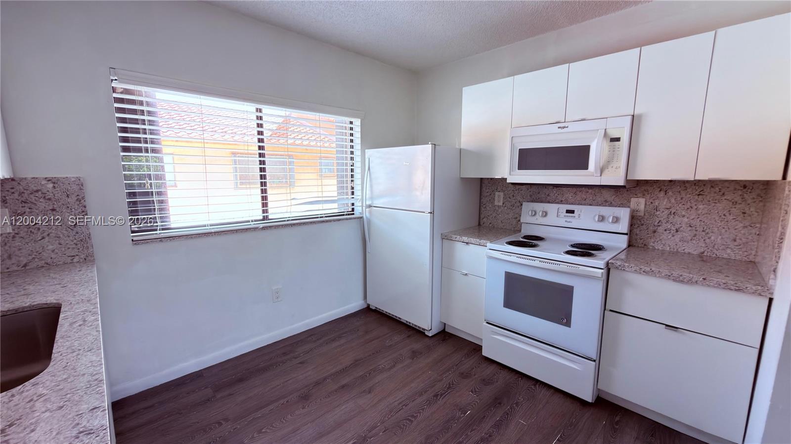 A kitchen features white appliances, white cabinets, and speckled countertops over dark wood-look flooring — 6370 W 27th Ct # 203, Hialeah FL 33016, HIALEAH, FL