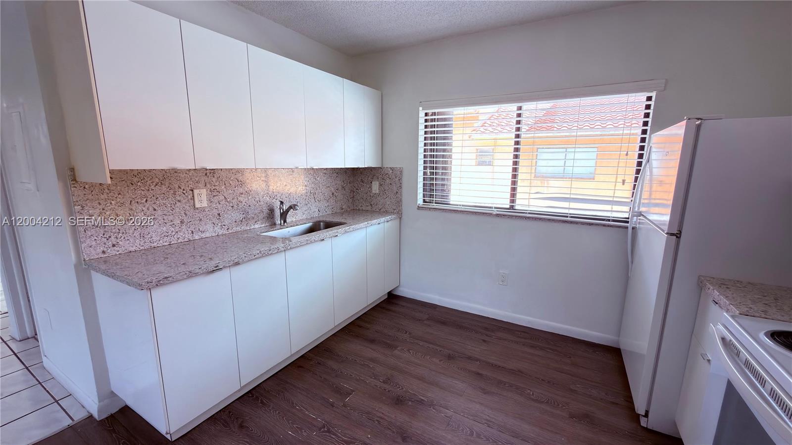 A kitchen features white cabinets, granite countertops, a stainless steel sink, and wood-look flooring — 6370 W 27th Ct # 203, Hialeah FL 33016, HIALEAH, FL