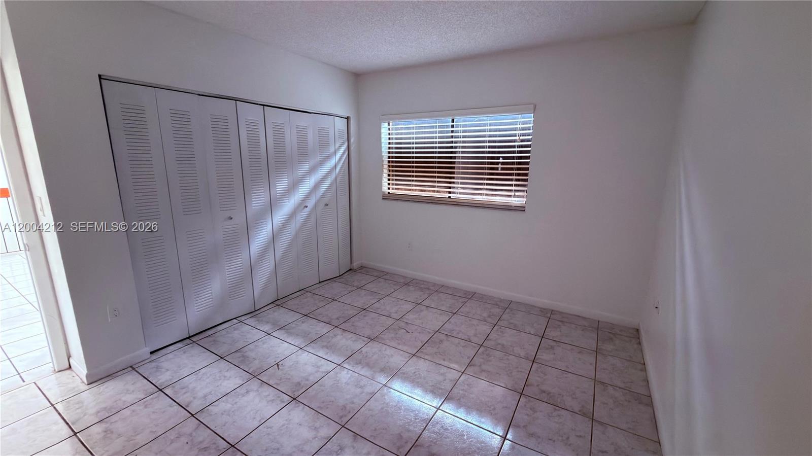 A bedroom features white walls, tiled flooring, a louvered closet, and a window with blinds — 6370 W 27th Ct # 203, Hialeah FL 33016, HIALEAH, FL