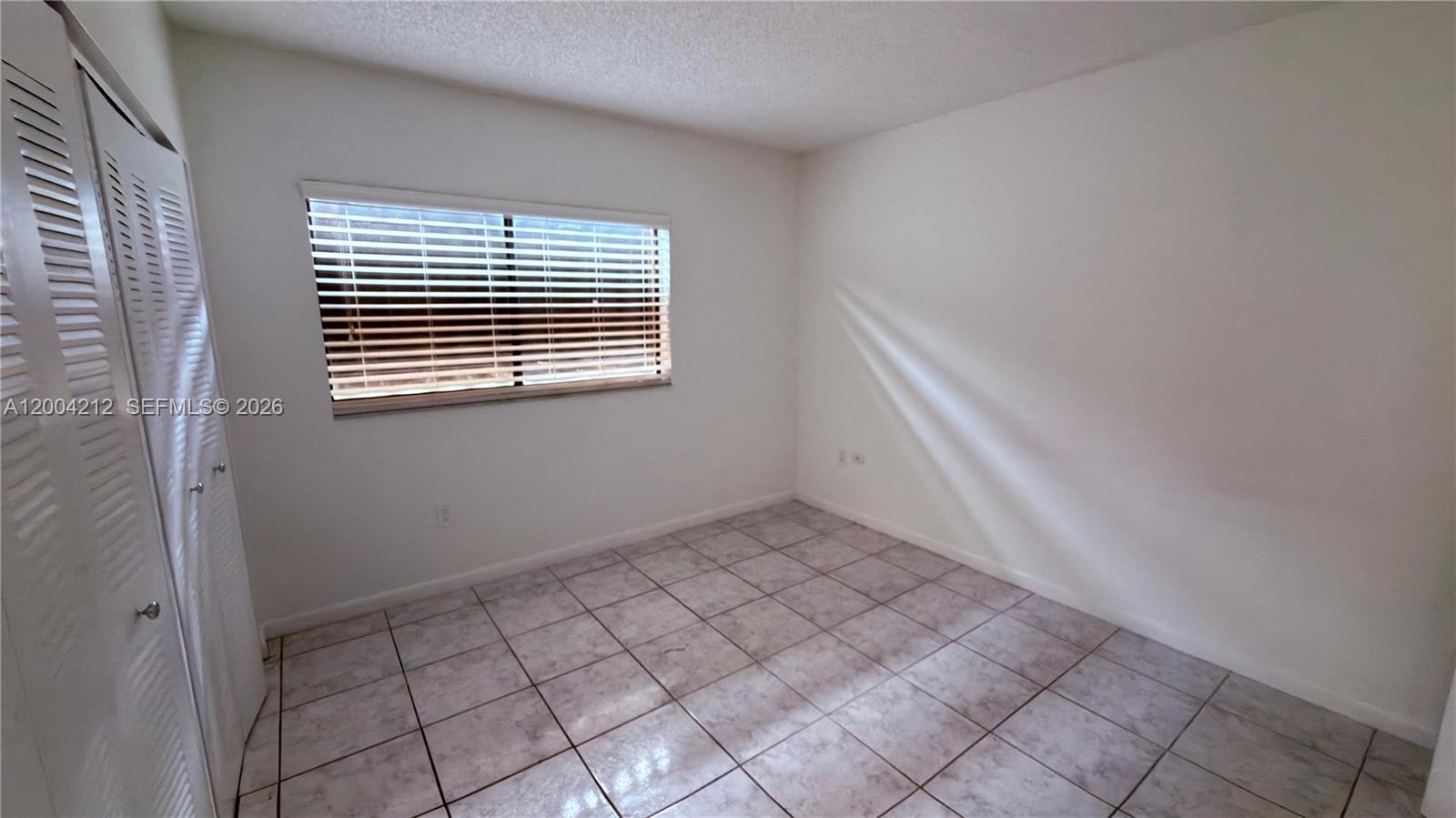 An empty bedroom features white walls, light-colored tile flooring, and a window with blinds — 6370 W 27th Ct # 203, Hialeah FL 33016, HIALEAH, FL