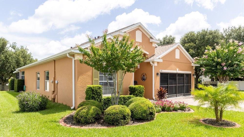 A single-story house with tan stucco walls, a screened garage, and landscaped front yard — 5911 WHISPER PINE DRIVE, LEESBURG, FL