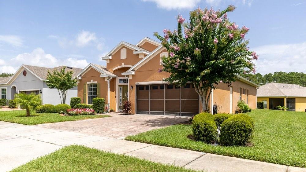 A tan stucco house with a brown garage and a blooming crape myrtle tree — 5911 WHISPER PINE DRIVE, LEESBURG, FL