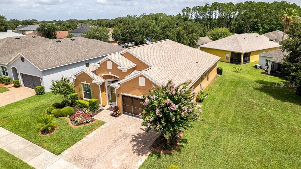 An aerial view shows a tan suburban house with a paved driveway and landscaped yard — 5911 WHISPER PINE DRIVE, LEESBURG, FL