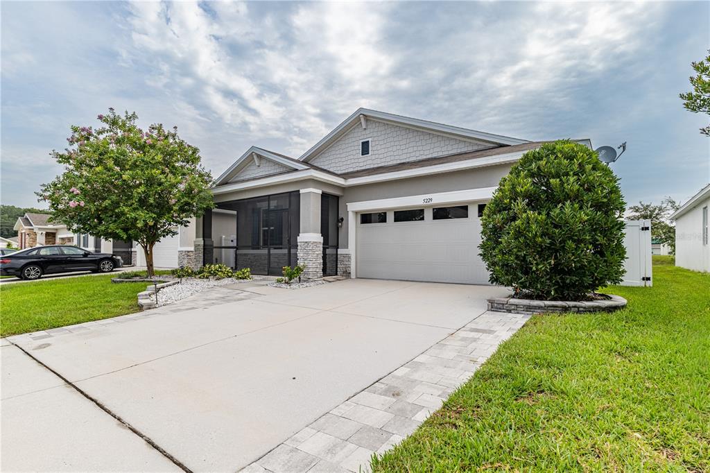A single-story house with a screened front porch, stone accents, and a flowering tree — 5229 MEADOW SONG DRIVE, OKAHUMPKA, FL