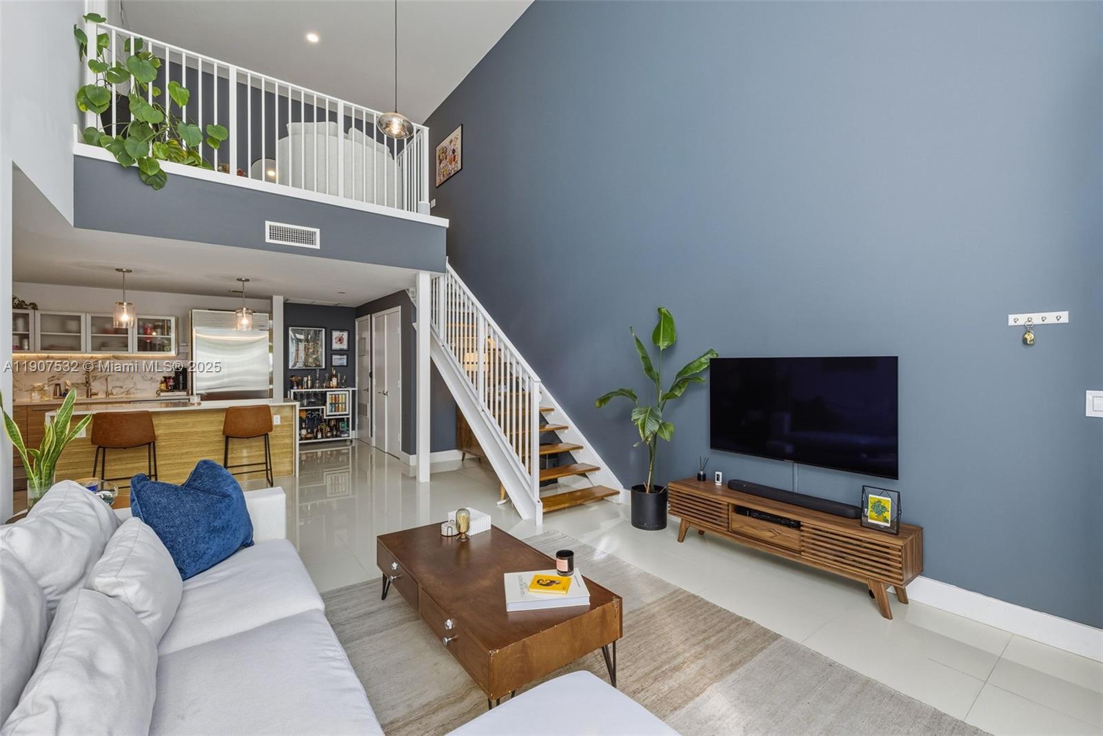 A living room with a high ceiling, blue accent wall, staircase, and open kitchen — 2020 N Bayshore, Miami FL 33137, MIAMI, FL