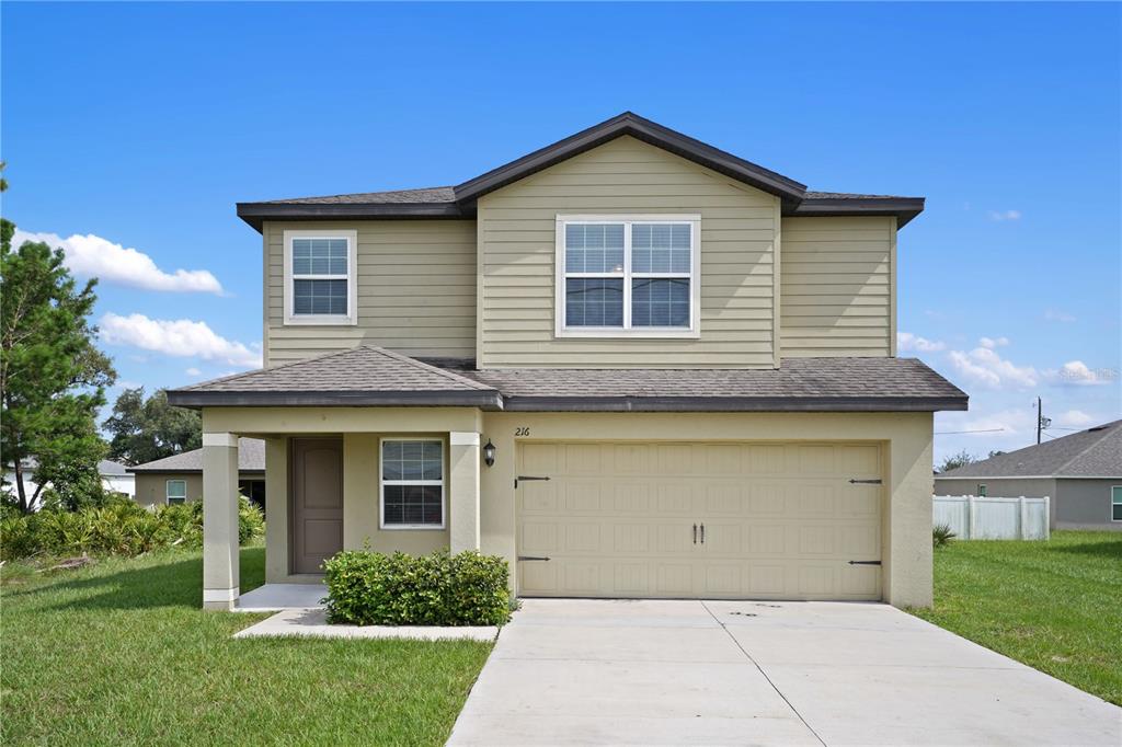 A two-story house with tan siding, a front porch, and an attached two-car garage — 216 FIG COURT, POINCIANA, FL