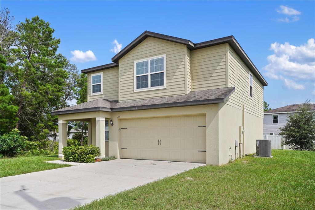 A two-story house with beige siding, a two-car garage, and a concrete driveway — 216 FIG COURT, POINCIANA, FL