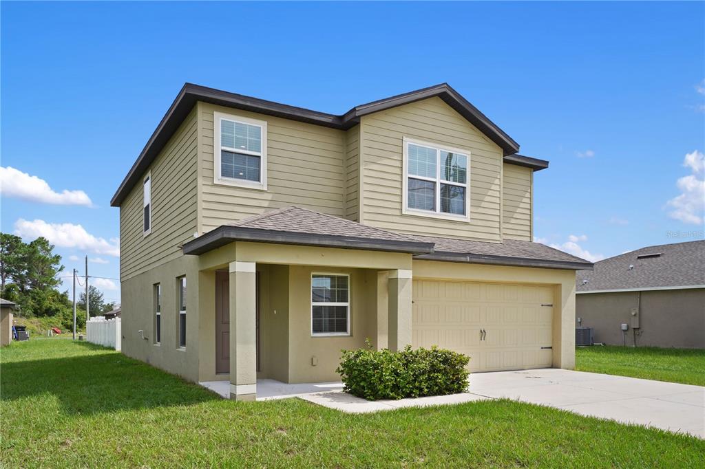 A two-story house with light green siding, a front porch, and an attached two-car garage — 216 FIG COURT, POINCIANA, FL