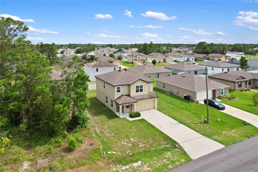 An aerial view of a two-story suburban house with a concrete driveway and adjacent woods — 216 FIG COURT, POINCIANA, FL