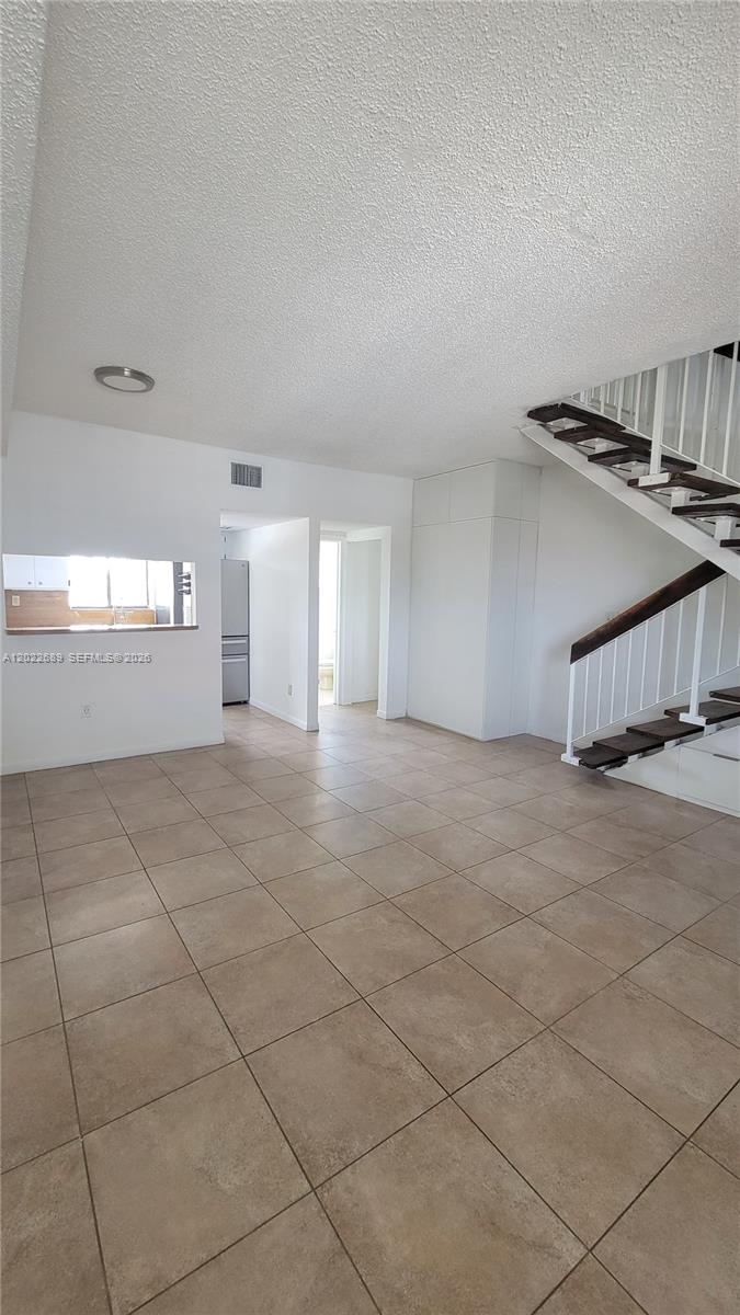 An open living area features a staircase, tile flooring, and a kitchen pass-through window — HIALEAH, FL