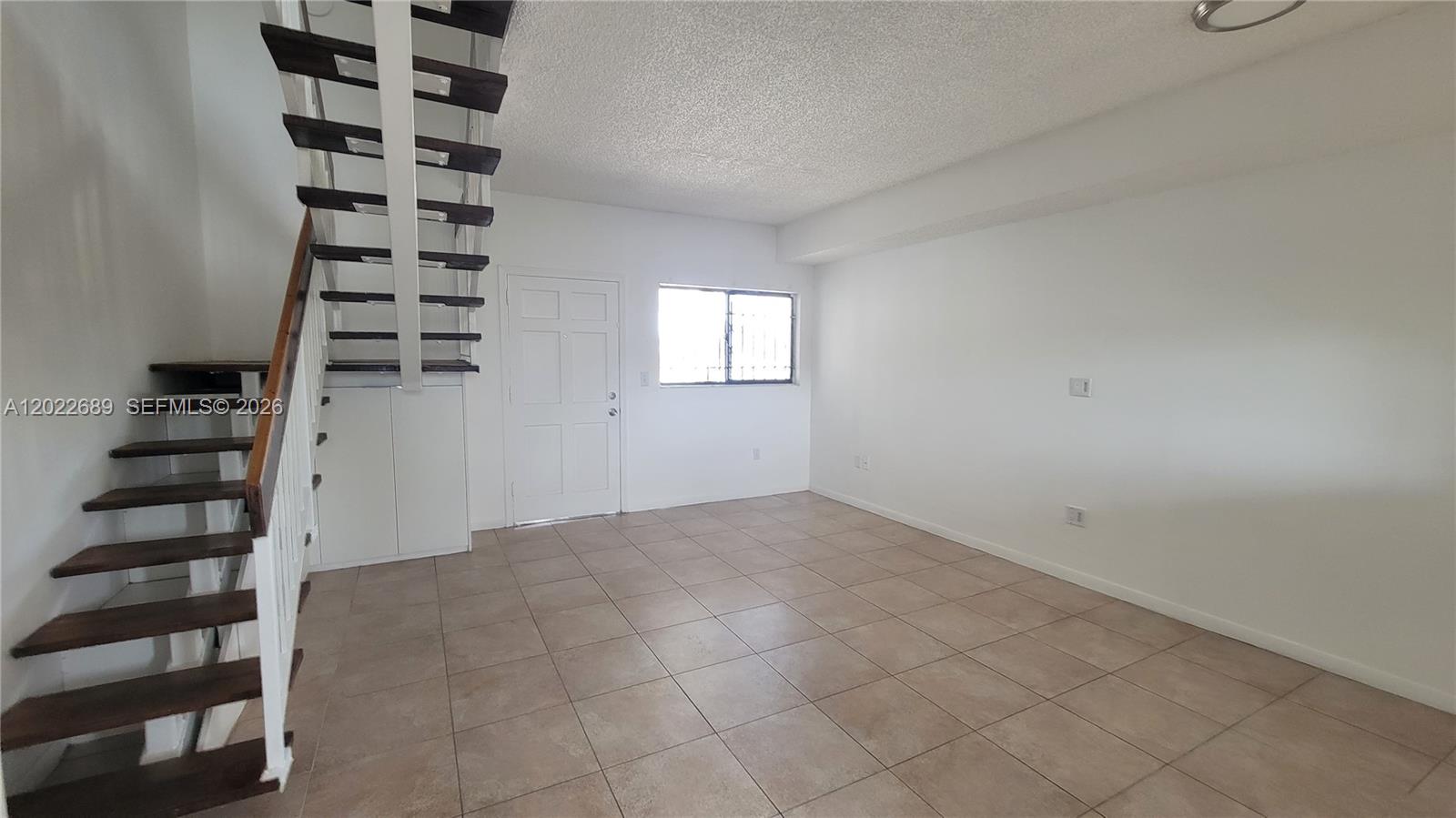 An empty room features tile flooring, white walls, and an open staircase with wooden treads — HIALEAH, FL