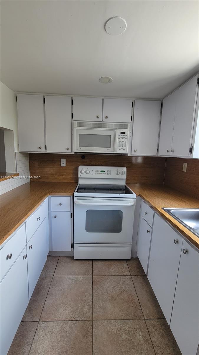 A kitchen features white cabinets, wood-look laminate countertops, a white stove, and tile flooring — HIALEAH, FL
