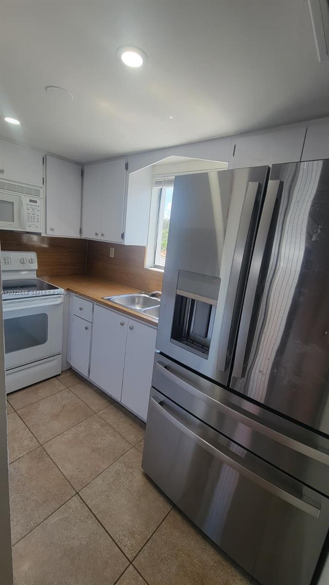 A kitchen features white cabinets, stainless steel appliances, wood countertops, and light-colored tile flooring — HIALEAH, FL