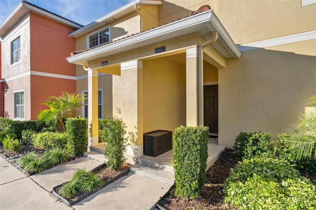 A yellow two-story townhouse exterior features a covered entryway with a black storage bin — 8957 SUGAR PALM ROAD, KISSIMMEE, FL