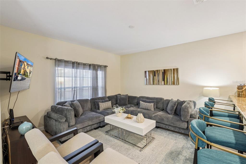 A living room features a large gray sectional sofa, a white coffee table, and bar stools — 8957 SUGAR PALM ROAD, KISSIMMEE, FL