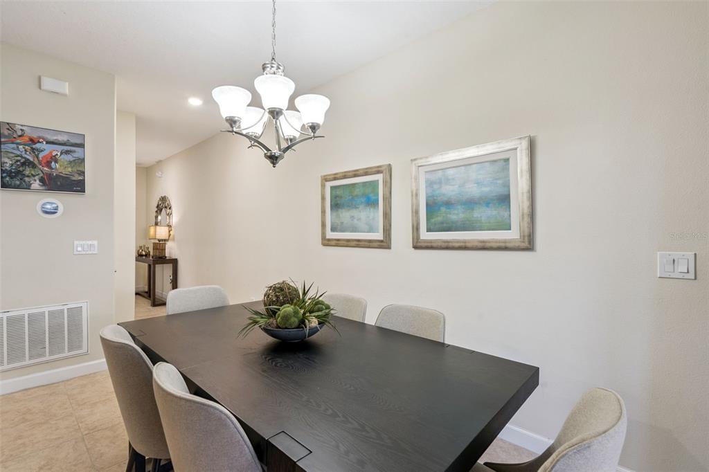 A dining room features a dark wood table, light gray chairs, and a chandelier — 8957 SUGAR PALM ROAD, KISSIMMEE, FL