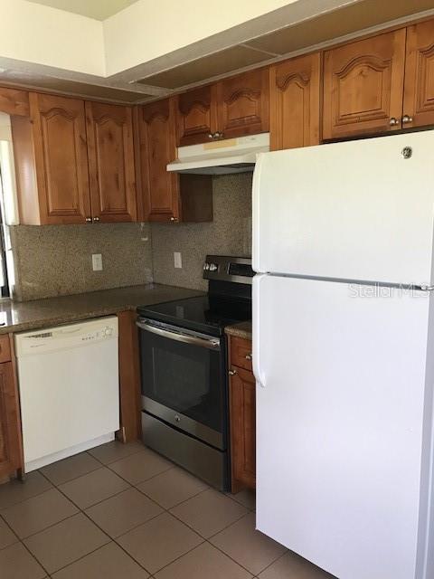 A kitchen features wood cabinets, stainless steel appliances, a white dishwasher, and tiled flooring — 25385 SANDHILL BOULEVARD UNIT E1, PUNTA GORDA, FL