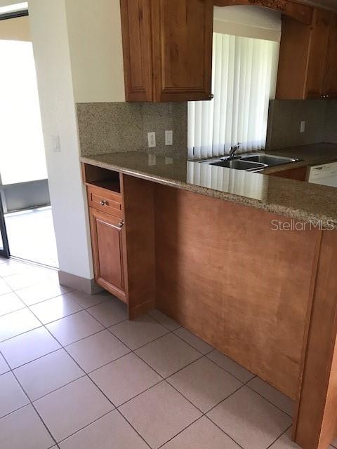 A kitchen features wood cabinets, a granite countertop, and a tiled floor — 25385 SANDHILL BOULEVARD UNIT E1, PUNTA GORDA, FL