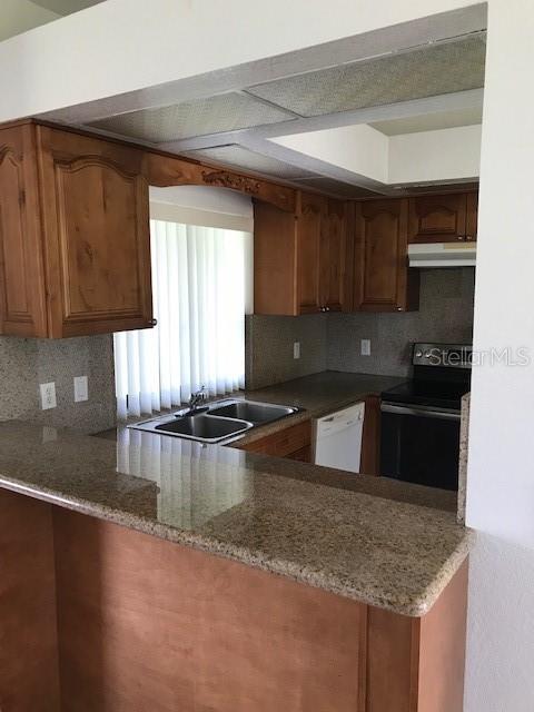 A kitchen features wood cabinets, granite countertops, a double sink, and a black stove — 25385 SANDHILL BOULEVARD UNIT E1, PUNTA GORDA, FL