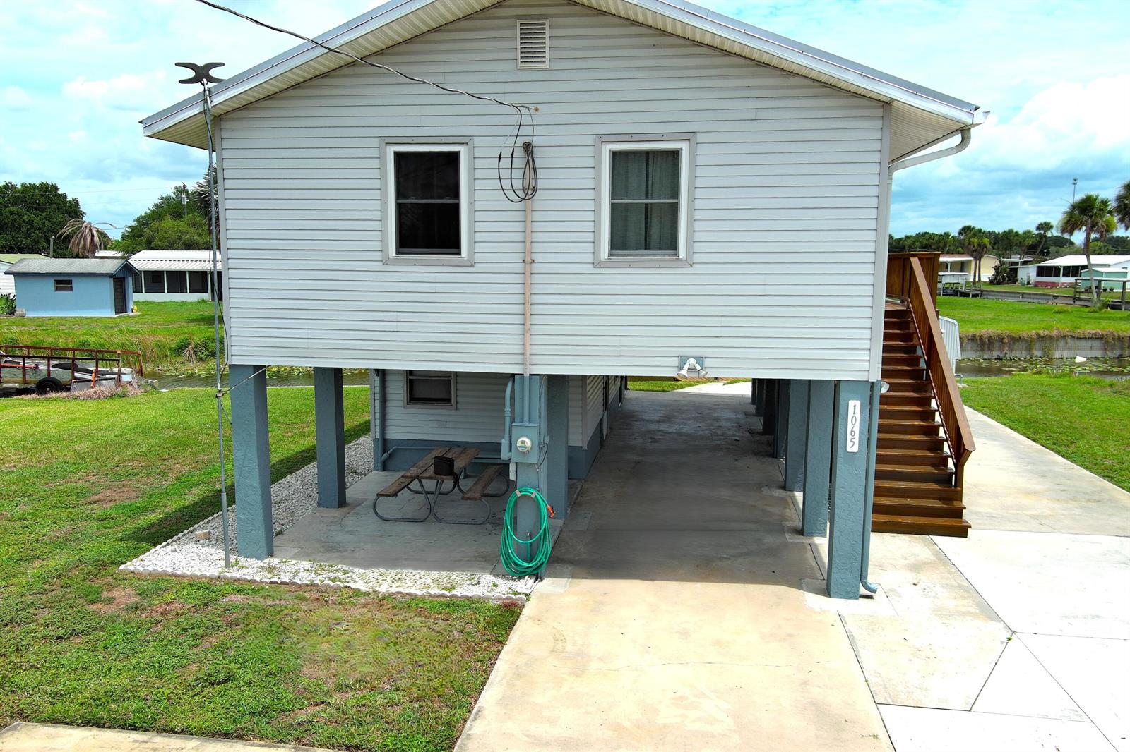 An elevated house with light gray siding, a concrete parking area, and wooden stairs — 1065 Peach Lane, Okeechobee FL 34974, OKEECHOBEE, FL