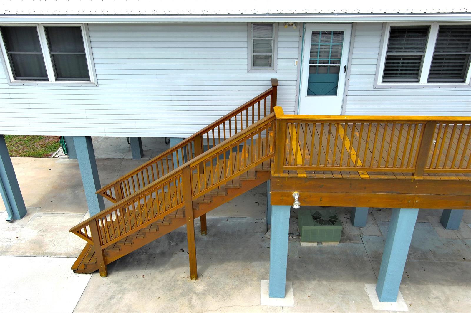 An elevated house features a wooden staircase leading to a deck supported by blue pillars — 1065 Peach Lane, Okeechobee FL 34974, OKEECHOBEE, FL