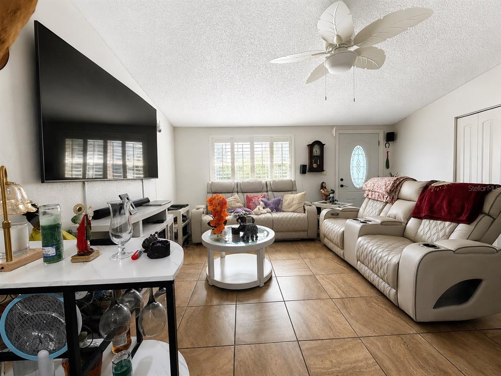 A living room features a large wall-mounted television, light-colored leather seating, and tiled flooring — 1341 FOXWOOD DRIVE, LUTZ, FL