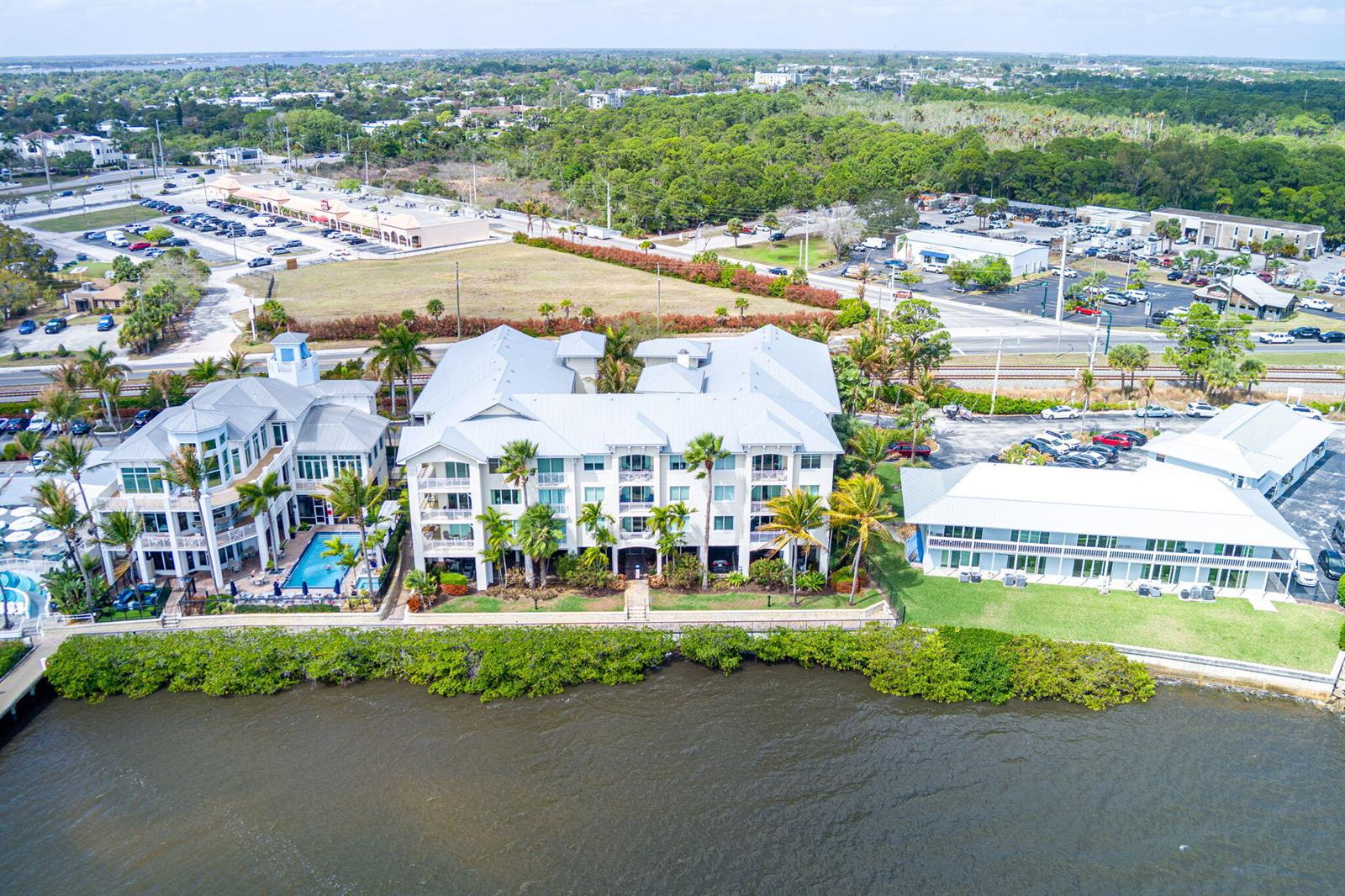 An aerial view shows three multi-story buildings situated along a waterfront with a swimming pool — 975 NW Flagler Avenue # 302, Stuart FL 34994, STUART, FL