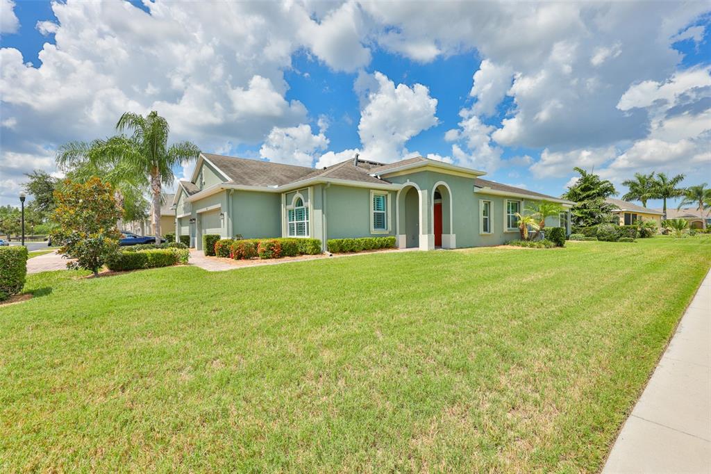A single-story green house with a tiled roof and arched entryway sits on a lawn — 803 CHIPPER DRIVE, SUN CITY CENTER, FL