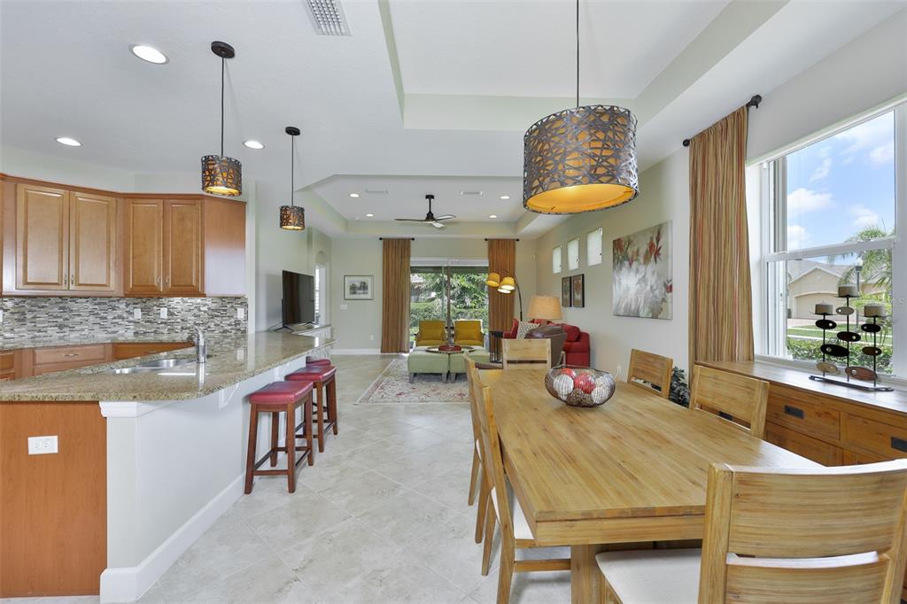 An open-concept kitchen and dining area with wood cabinets, granite countertops, and tile flooring — 803 CHIPPER DRIVE, SUN CITY CENTER, FL