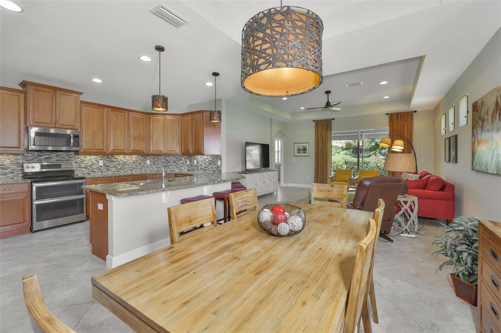 An open-concept kitchen and dining area featuring wooden cabinets, granite countertops, and tile flooring — 803 CHIPPER DRIVE, SUN CITY CENTER, FL