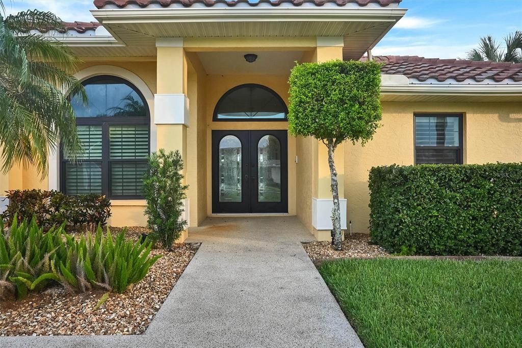 The exterior of a yellow house features a concrete walkway leading to double front doors — 1565 WATERFORD DRIVE, VENICE, FL