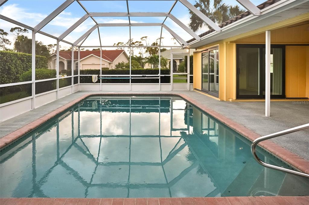 A rectangular swimming pool is enclosed by a screened lanai next to a yellow house — 1565 WATERFORD DRIVE, VENICE, FL