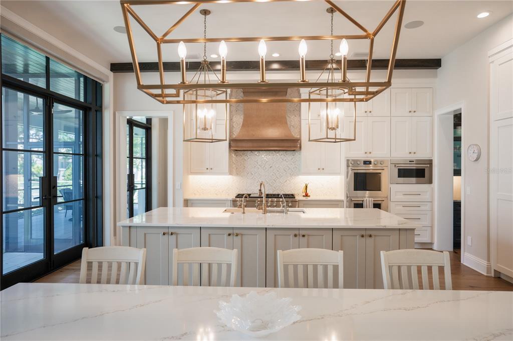 A bright kitchen features white cabinetry, a large marble-topped island, and dark wood ceiling beams — 4402 W BEACH PARK DRIVE, TAMPA, FL