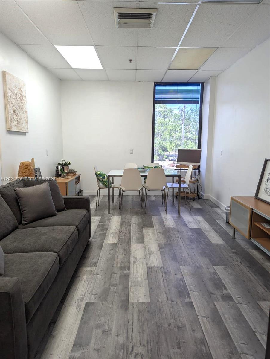 A living and dining area features gray wood-look flooring, white walls, and a large window — 12550 Biscayne Blvd # 220, North Miami FL 33181, NORTH MIAMI, FL