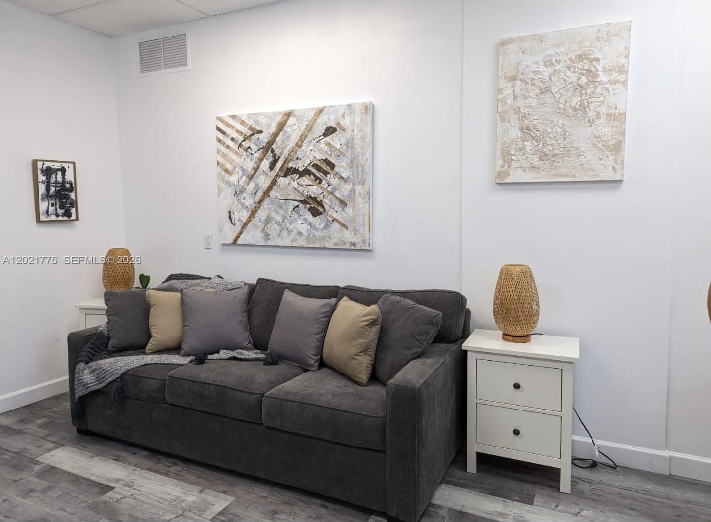 A gray sofa sits against a white wall decorated with three pieces of abstract art — 12550 Biscayne Blvd # 220, North Miami FL 33181, NORTH MIAMI, FL