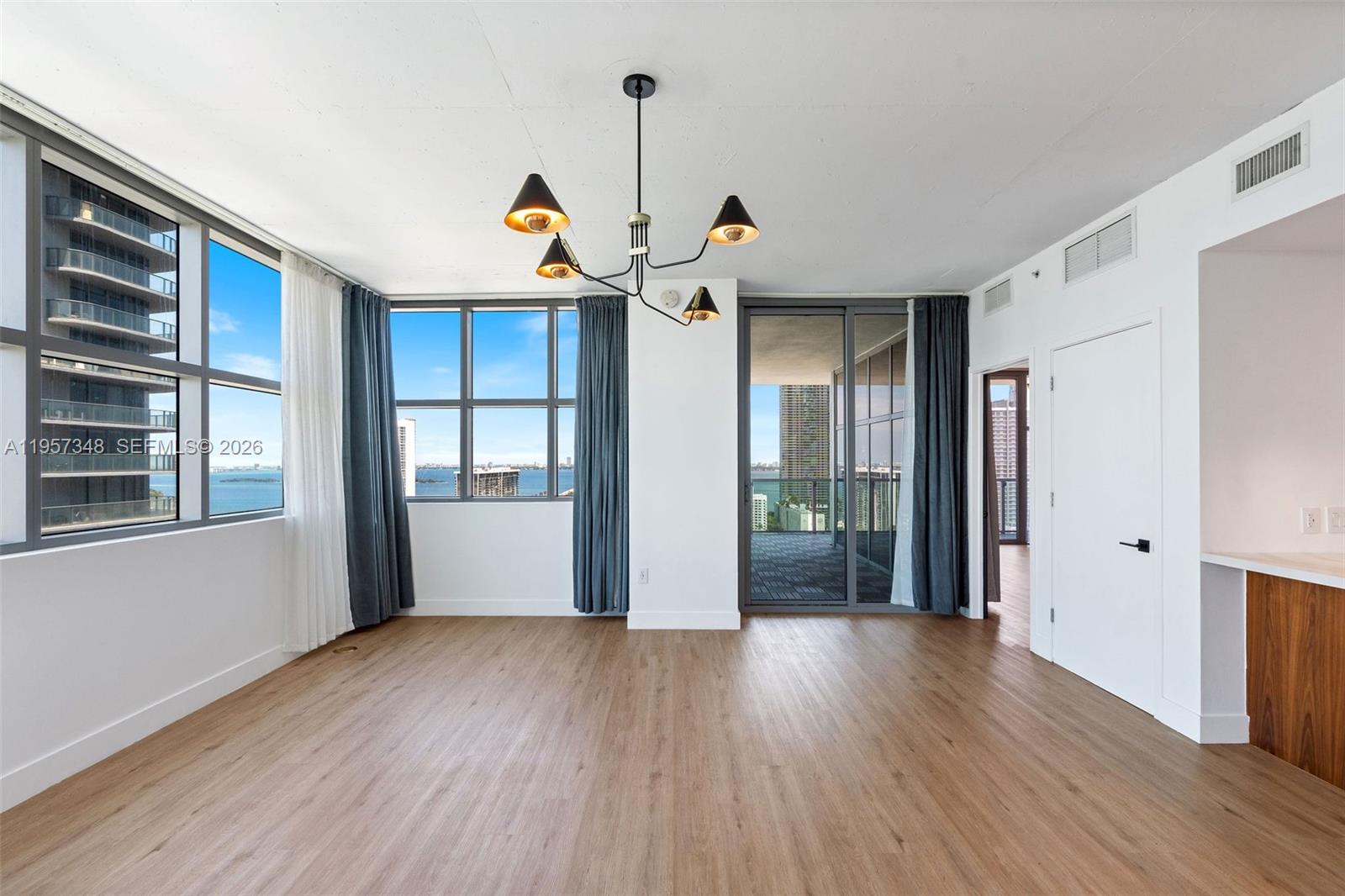 An empty living room features wood-look flooring, a modern chandelier, and floor-to-ceiling windows with water views — 3301 NE 1st Ave # H2215, Miami FL 33137, MIAMI, FL