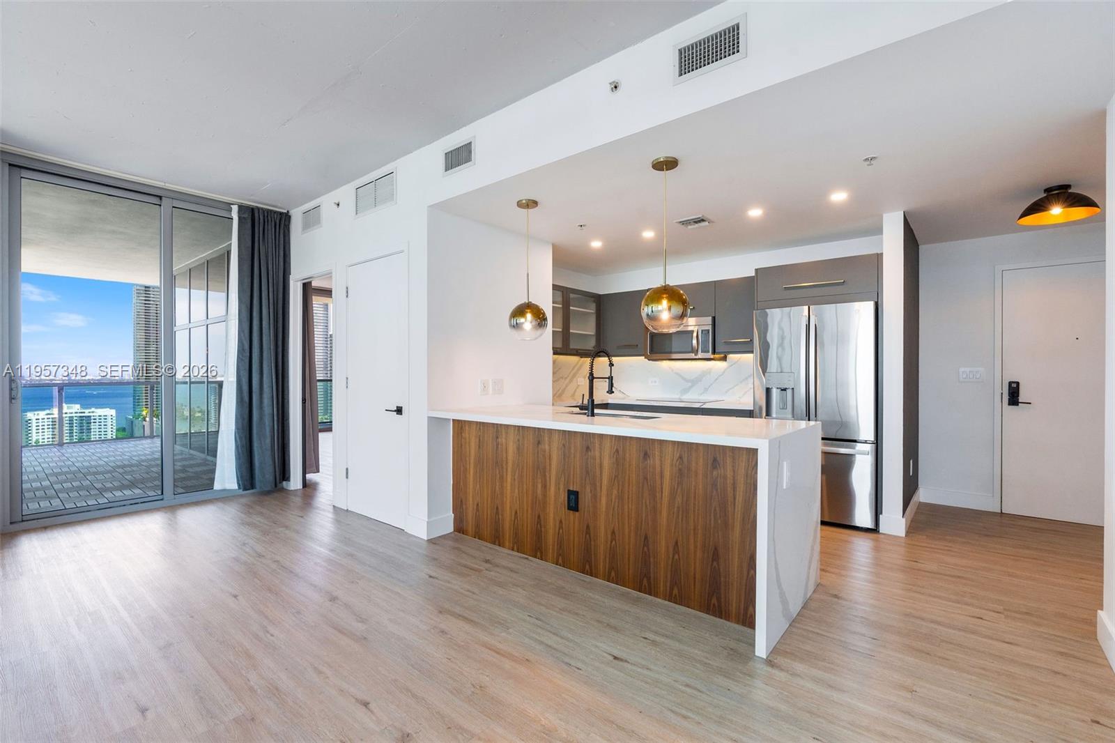A modern kitchen features a wood-paneled island, white countertops, and a balcony with ocean views — 3301 NE 1st Ave # H2215, Miami FL 33137, MIAMI, FL