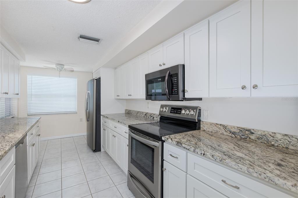 A kitchen with white cabinets, granite countertops, stainless steel appliances, and light tile flooring — 1148 FERNWOOD DRIVE, HOLIDAY, FL