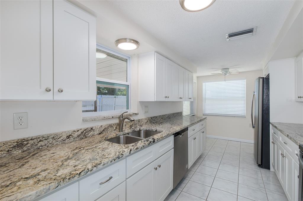 A kitchen featuring white cabinets, granite countertops, stainless steel appliances, and light-colored tile flooring — 1148 FERNWOOD DRIVE, HOLIDAY, FL