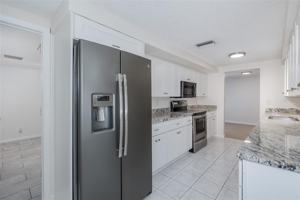 A kitchen with white cabinets, granite countertops, stainless steel appliances, and light tile flooring — 1148 FERNWOOD DRIVE, HOLIDAY, FL