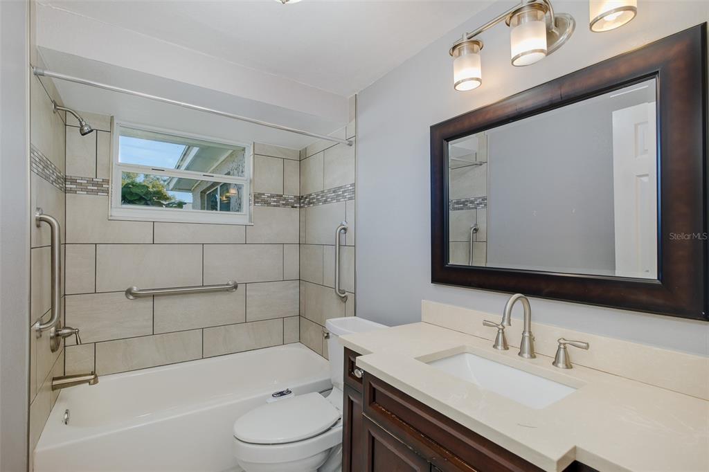 A bathroom features a tiled tub-shower combination, a dark wood vanity, and a framed mirror — 1148 FERNWOOD DRIVE, HOLIDAY, FL