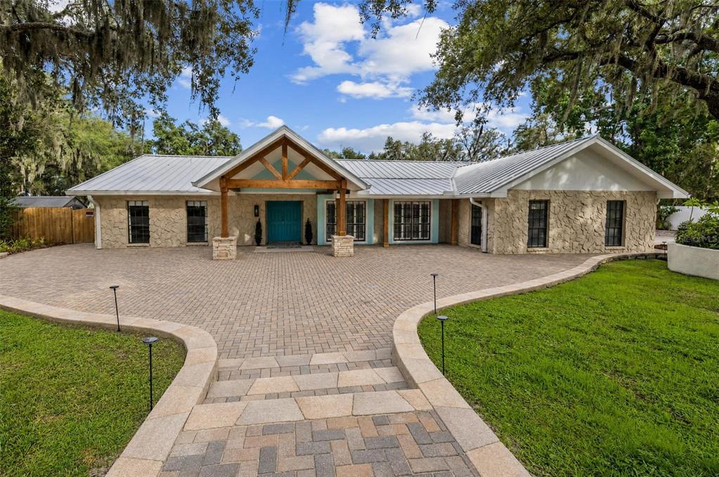 A single-story house with a stone facade, metal roof, and a paved circular driveway — 11310 DONNEYMOOR DRIVE, RIVERVIEW, FL