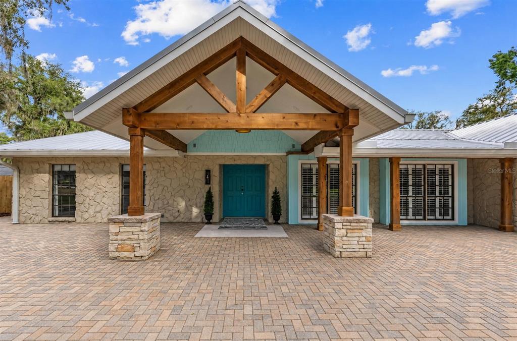 A stone-clad house exterior features a large wooden timber-framed portico over a blue front door — 11310 DONNEYMOOR DRIVE, RIVERVIEW, FL
