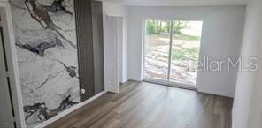 A room with wood-look flooring, a marble-patterned accent wall, and sliding glass doors to outside — 1152 NE 9 STREET, OCALA, FL