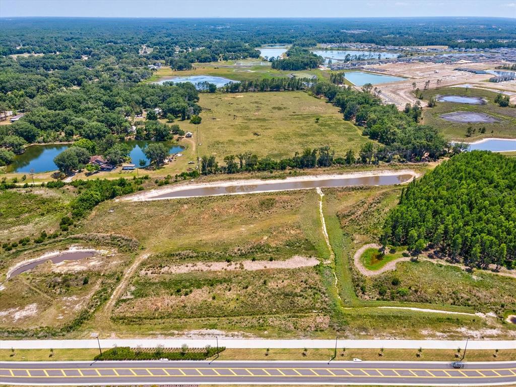 An aerial view shows a large, undeveloped grassy lot bordering a road and several ponds — 8989 EHREN CUTOFF, LAND O LAKES, FL