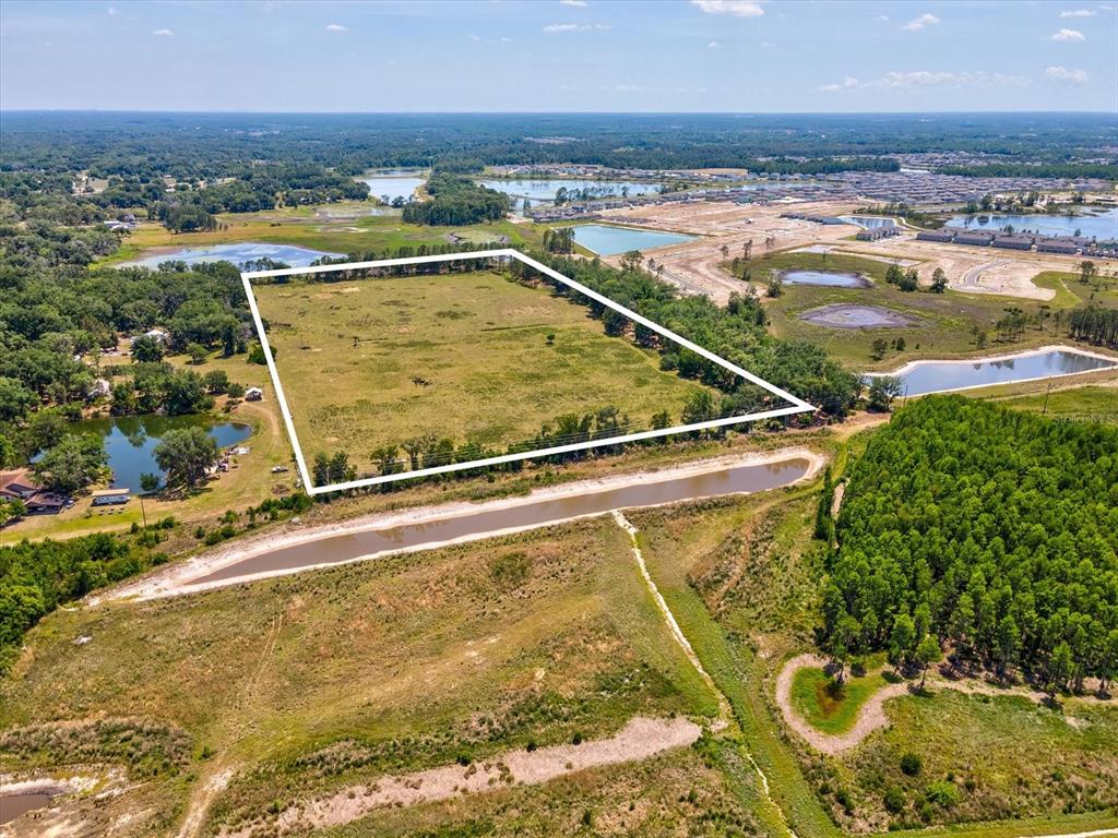 An aerial view shows a large, rectangular grassy plot outlined in white near water — 8989 EHREN CUTOFF, LAND O LAKES, FL