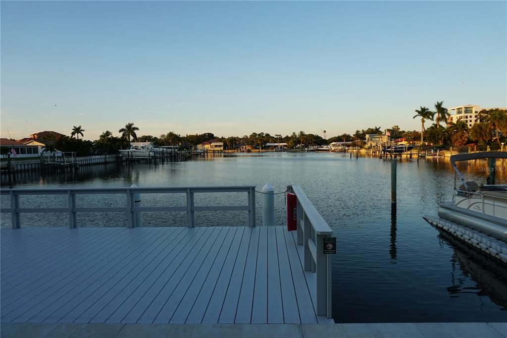 A wooden dock overlooks a calm canal lined with houses, palm trees, and docked boats — 3753 46TH AVENUE S UNIT 12, ST PETERSBURG, FL