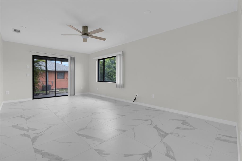 An empty room features white marble-patterned tile flooring, a ceiling fan, and sliding glass doors — 6359 HERA STREET UNIT B, ENGLEWOOD, FL